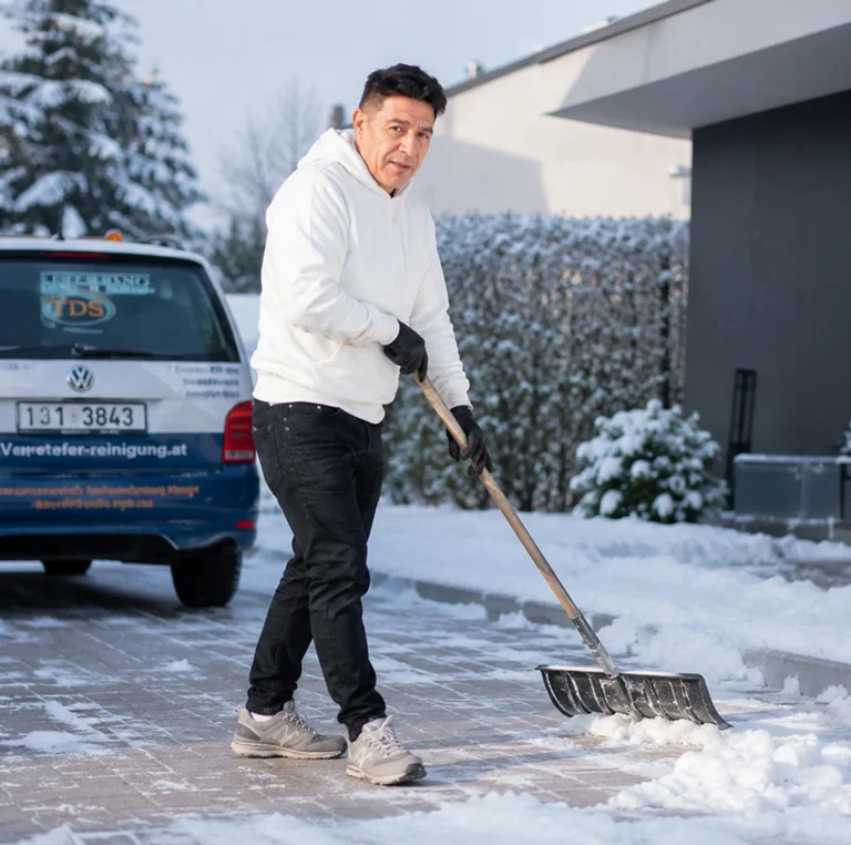 Winterdienst Mitarbeiter räumt Schnee vor Gebäude in Wien mit Schneeschaufel – Gehwegreinigung durch Schiefer GmbH